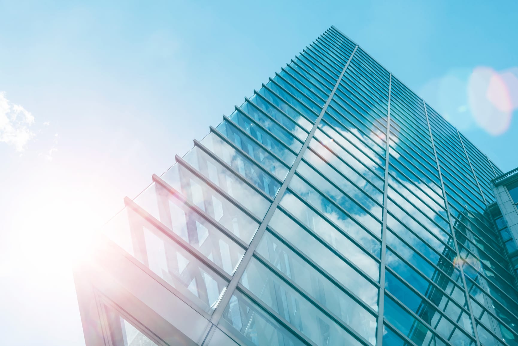 Glass sharp angled office building shot from low angle with sun shining from bottom left corner behind building.